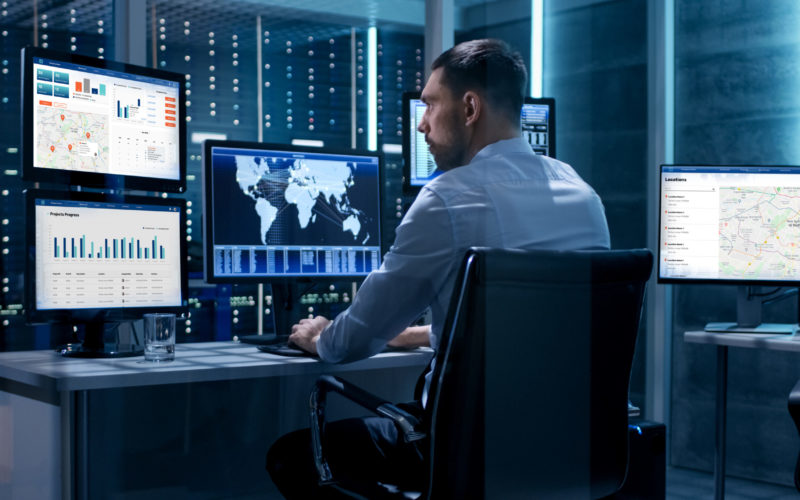 Technical Controller Working at His Workstation with Multiple Displays. Displays Show Various Technical Information. He's Alone in System Control Center.