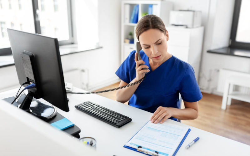 medicine, technology and healthcare concept - female doctor or nurse with computer and clipboard calling on phone at hospital