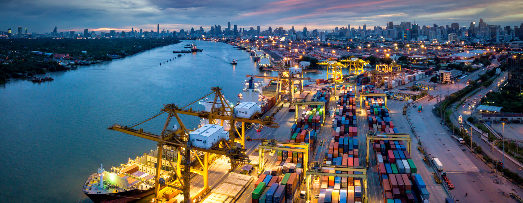 Aerial view of international port with Crane loading containers in import export business logistics with cityscape of Bangkok city Thailand at night